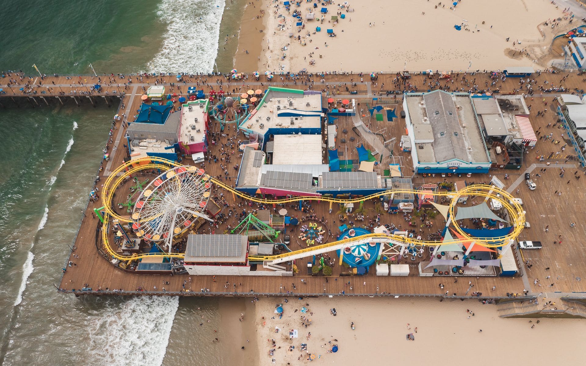A family walking along the wide wooden pier at Santa Cruz Beach Boardwalk with the roller coaster behind them