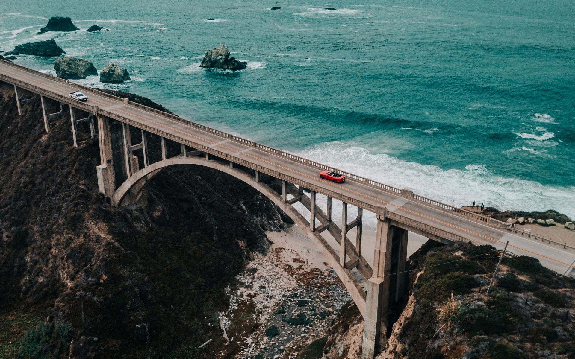 A rental car pulled over at a Highway 1 overlook above the ocean near Big Sur, coast curving into the distance