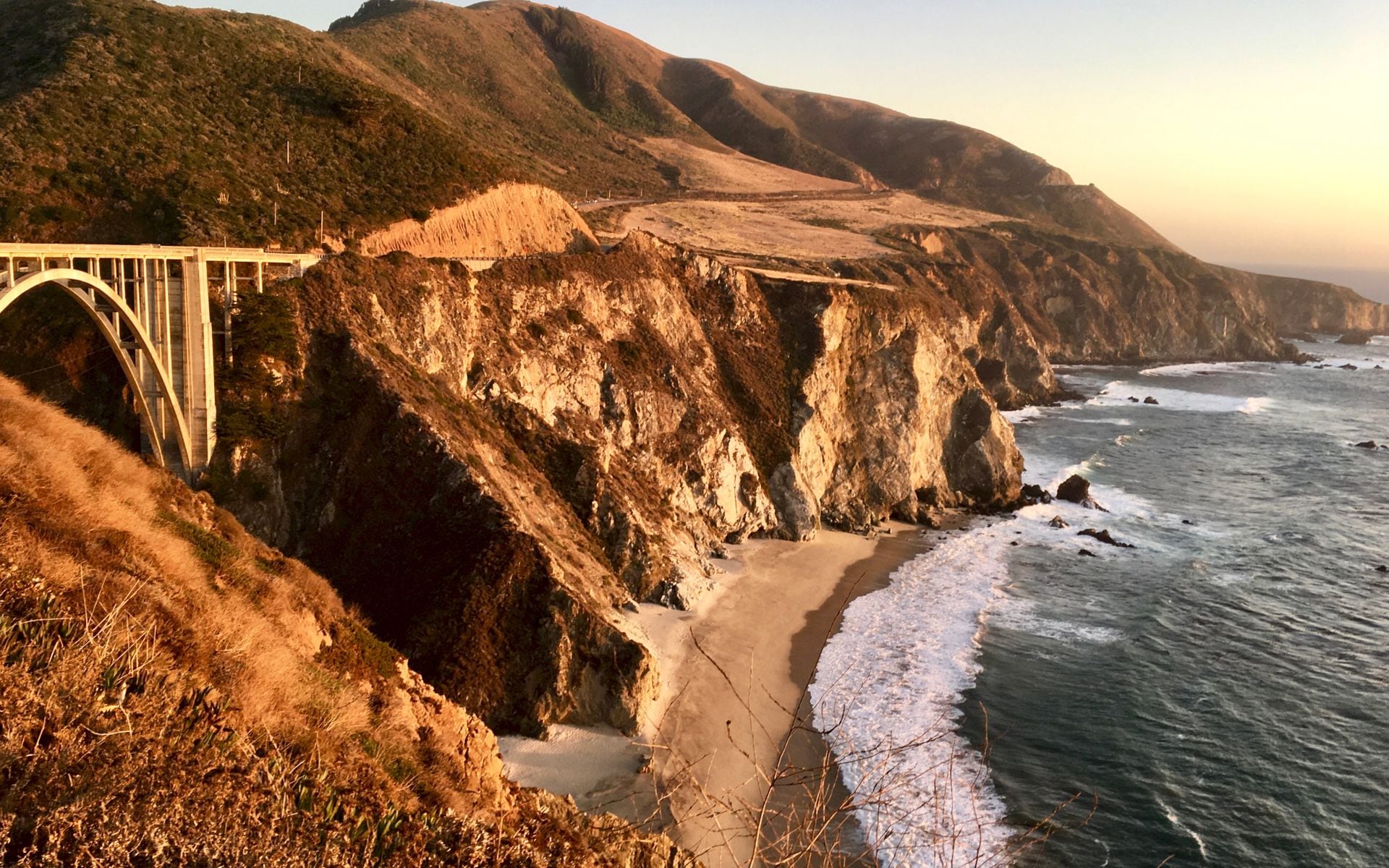 A red convertible parked at a Highway 1 overlook above the Pacific near Big Sur at golden hour