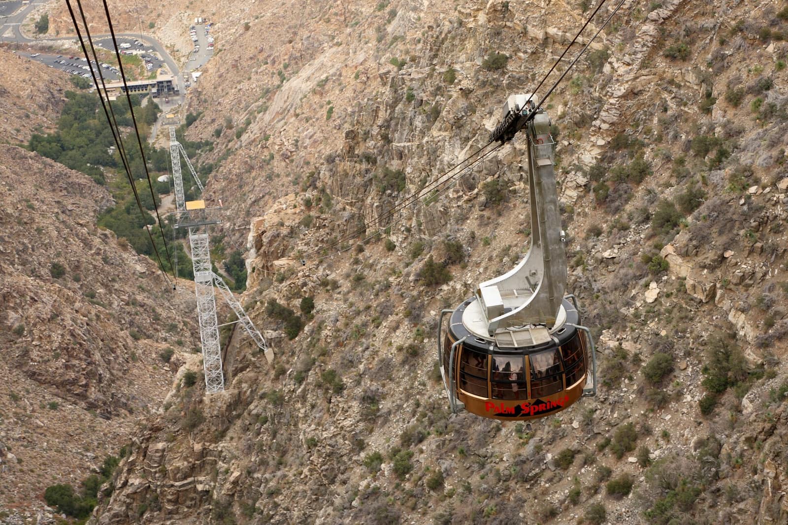 Palm Springs Aerial Tramway cable car ascending over rocky desert terrain above Chino Canyon, with the valley station visible below