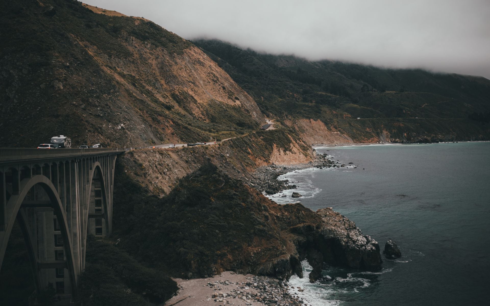 A rental convertible parked at a coastal pullout on Highway 1 in Big Sur with the Pacific Ocean and cliffs in the background.